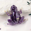 A purple crystal frog resin craft decoration lying on a white surface.