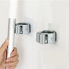 A hand is installing an adhesive wall hook for mops and brushes onto a white wall.