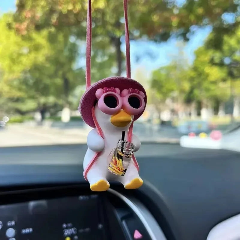 A cute pink anime duck swing mirror ornament hanging from a string is visible in a car interior.