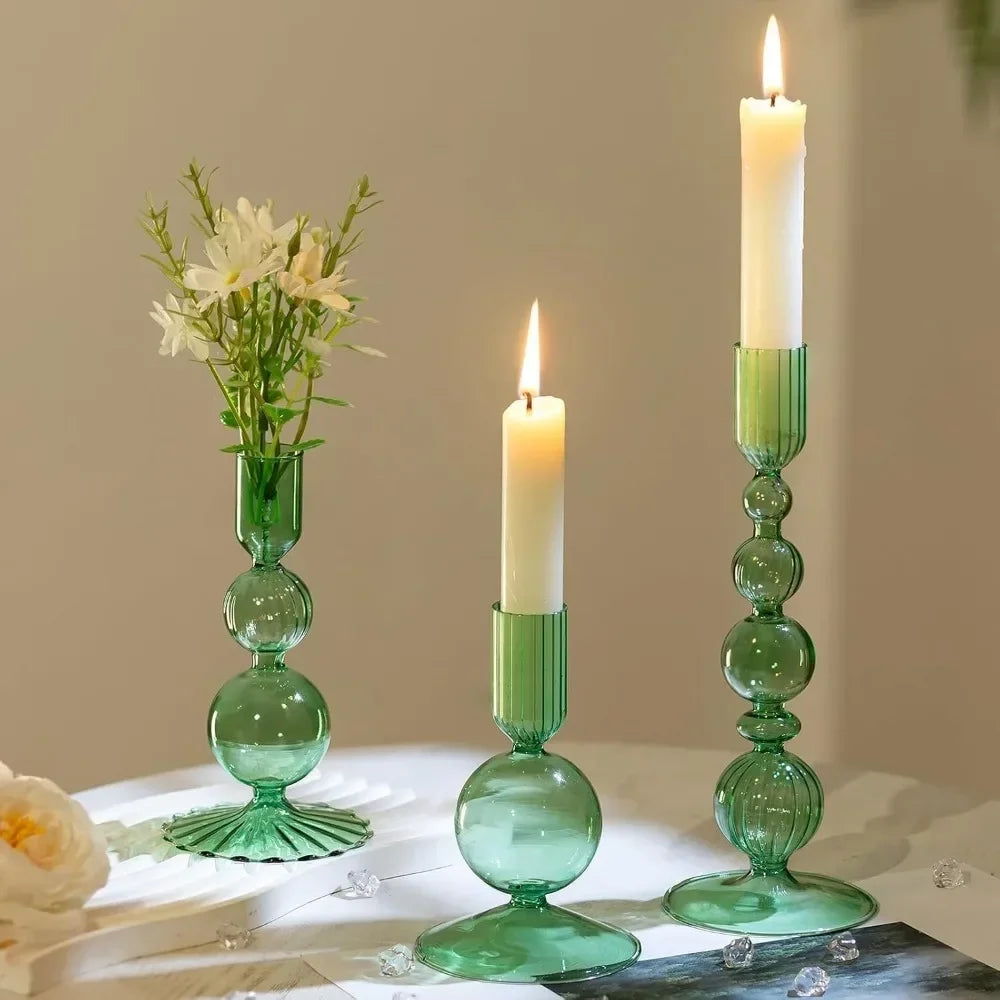 A set of three groovy wavy glass taper candle holders with green candles and flowers on a white surface.