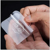 A hand holds a transparent self-adhesive wall hook, showing its clear plastic and textured surface.