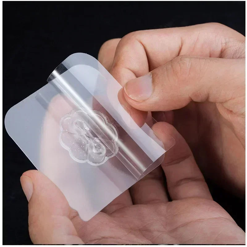 A hand holds a transparent self-adhesive wall hook, showing its clear plastic and textured surface.