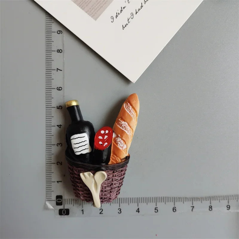 A set of playful food-shaped fridge magnets including a bottle, a strawberry, and a croissant, arranged next to a ruler.