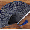 A dark blue folding hand fan with a repeating wave pattern is displayed on a wooden surface.
