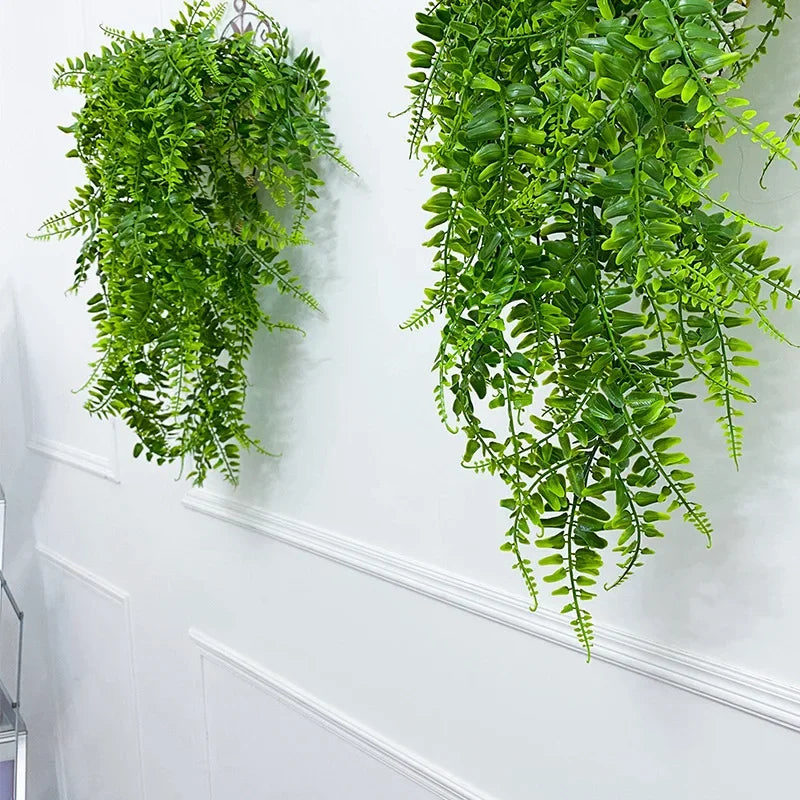 Disposition verticale de plantes suspendues en rotin vert artificiel décorant un mur blanc.