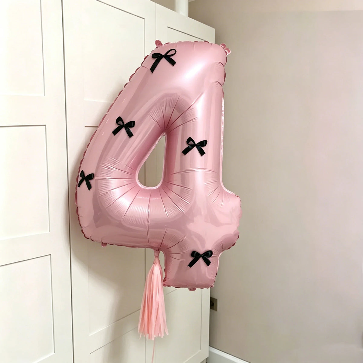 A pink foil balloon shaped like the number 4 with black bows, hanging on a white door frame.