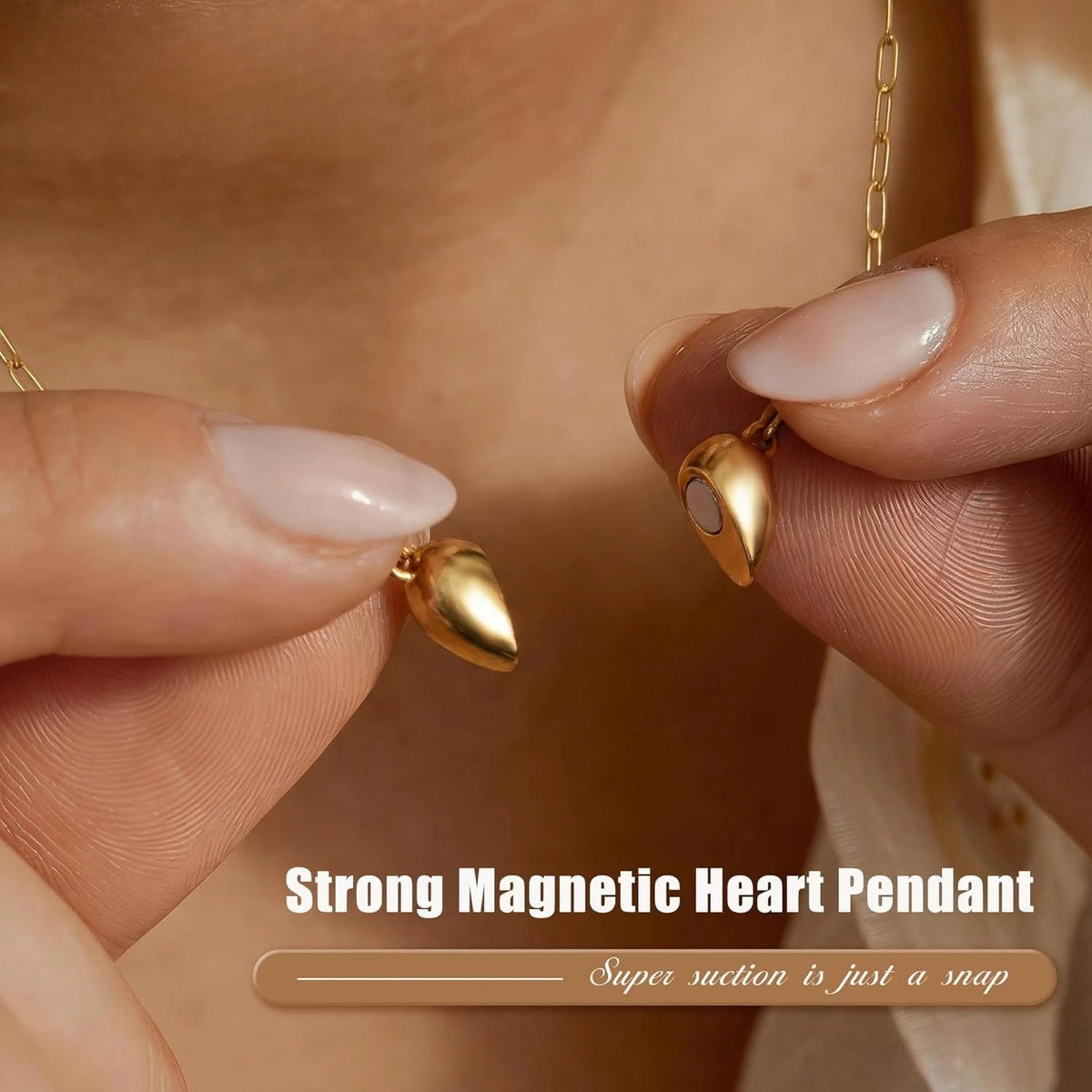 A close-up shot of a gold plated heart pendant necklace being held by a hand, showing the magnetic clasp mechanism.