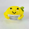 A yellow knitted plush doll shaped like a lemon with a green top, smiling and featuring embroidered eyes and mouth.