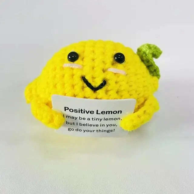 A yellow knitted plush doll shaped like a lemon with a green top, smiling and featuring embroidered eyes and mouth.