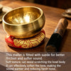 A golden copper singing bowl resting on a red fabric, next to a wooden mallet.