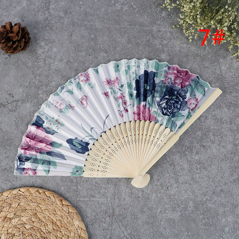 A hand carved bamboo folding fan with a floral and botanical pattern displayed on a gray surface.
