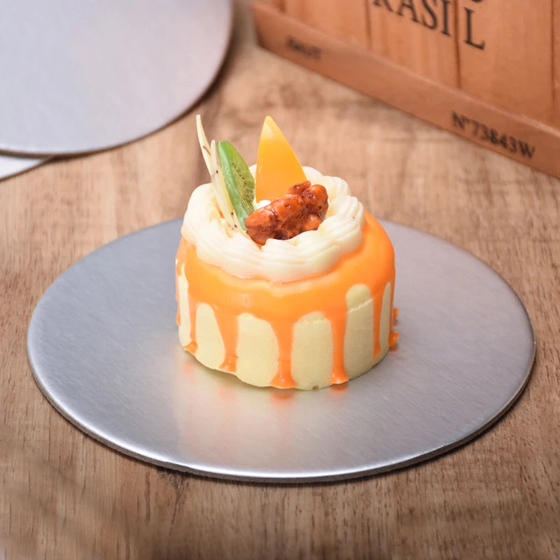 A small orange and white layered dessert with a cream topping and a garnish on a silver cake board.