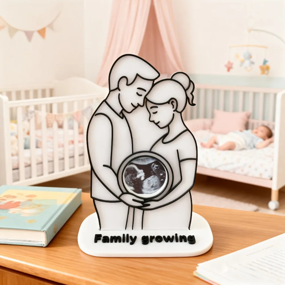 A white silhouette of a mother and baby embracing, holding an ultrasound photo, on a wooden table.