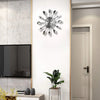 A modern cutlery 3D wall clock with silver utensils mounted on a white wall above a television and plant.