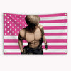 A muscular man in a tank top and jeans stands against a pink and white striped American flag banner.