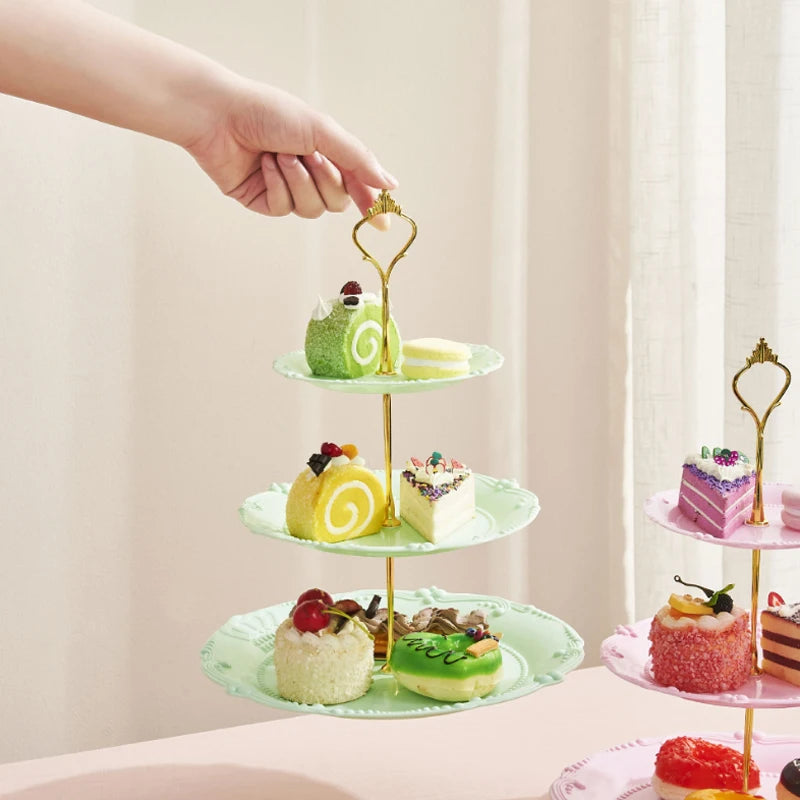 A hand is placing cupcakes on a three-tiered plastic stand decorated with green and yellow frosting.
