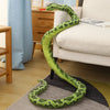A bright green, realistic snake plush toy is coiled on a gray rug next to a light-colored sofa.