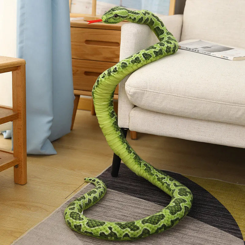 A bright green, realistic snake plush toy is coiled on a gray rug next to a light-colored sofa.