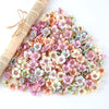 A pile of silk artificial flower heads in shades of pink, peach, and blue scattered on a white surface.
