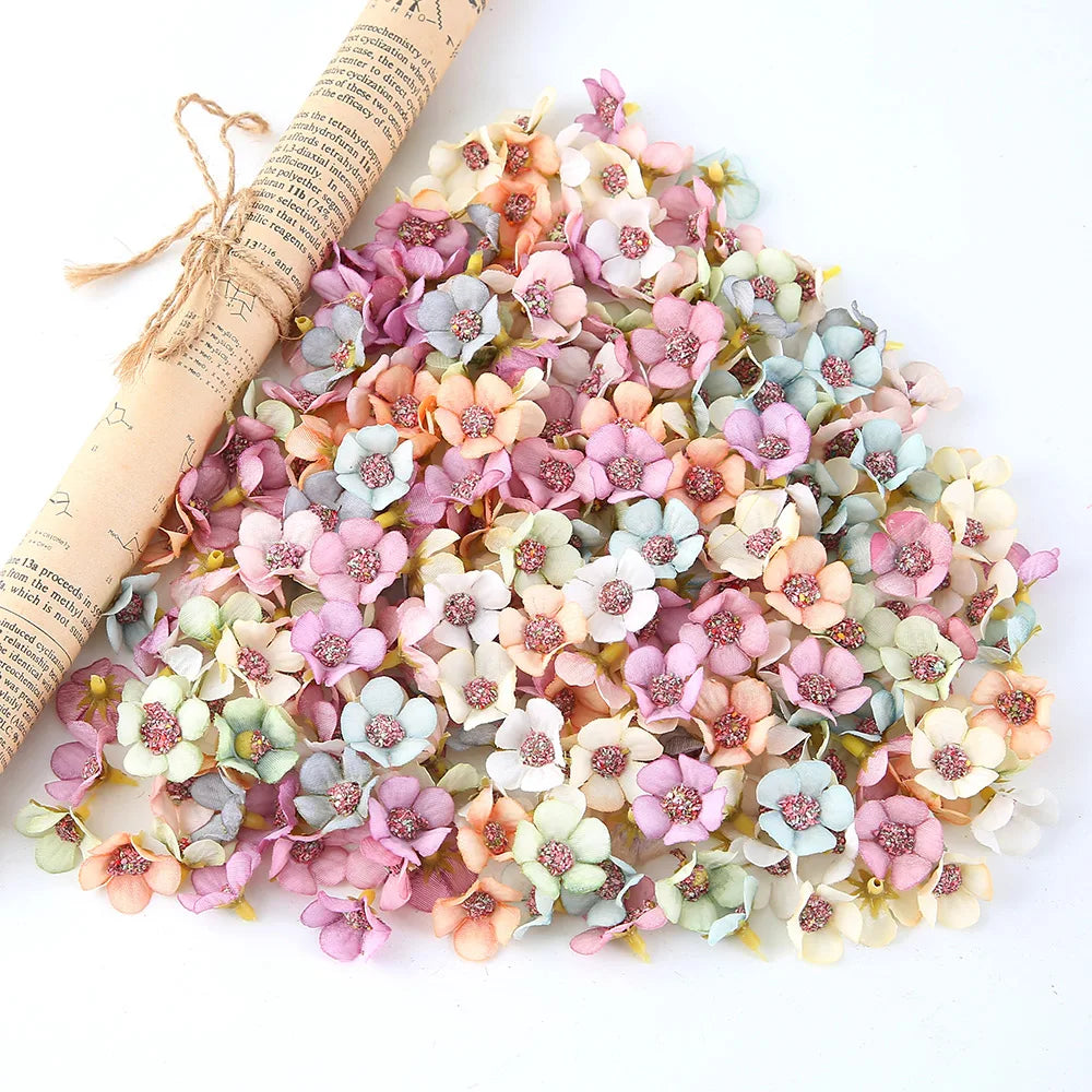 A pile of silk artificial flower heads in shades of pink, peach, and blue scattered on a white surface.