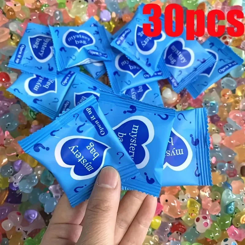 A hand holds a stack of blue glow in the dark resin decor bags with heart shapes on a background of colorful resin pieces.