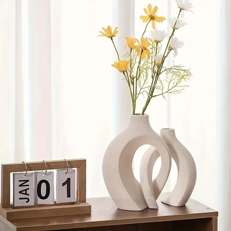 A set of two white ceramic vases in an organic, modern design holding yellow and white flowers.