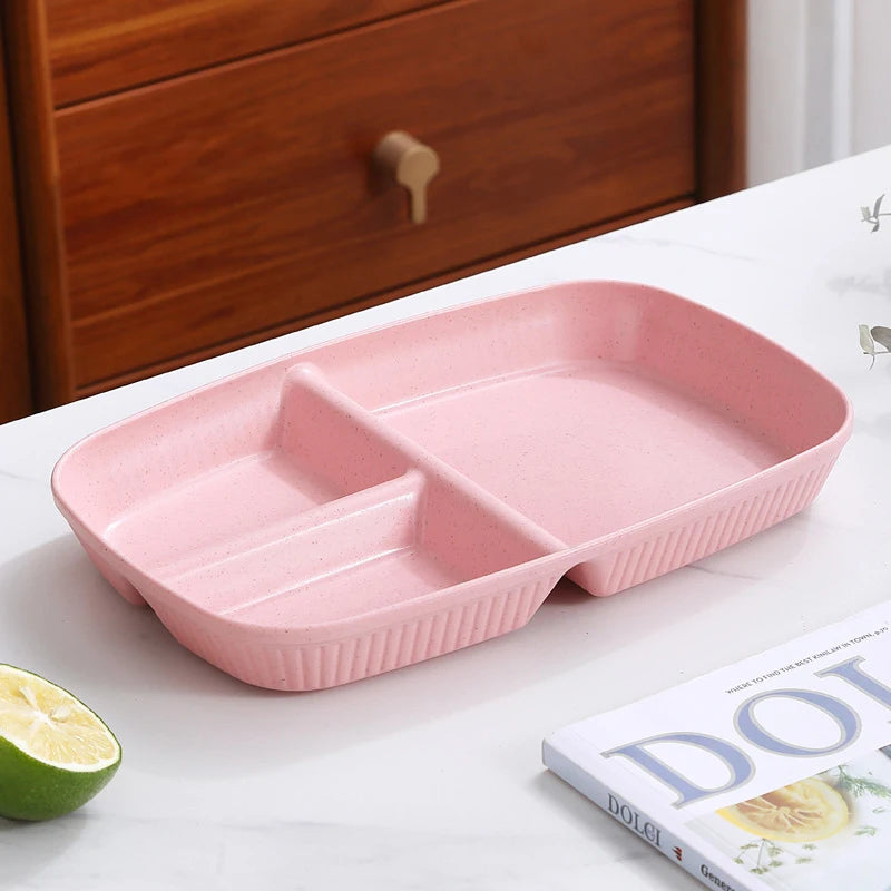 A pink 3-compartment portion control plate is displayed on a white surface next to a lime and a book.