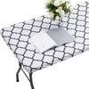A white and gray patterned elastic fitted rectangle tablecloth is displayed on a table, with a stack of white papers and a va