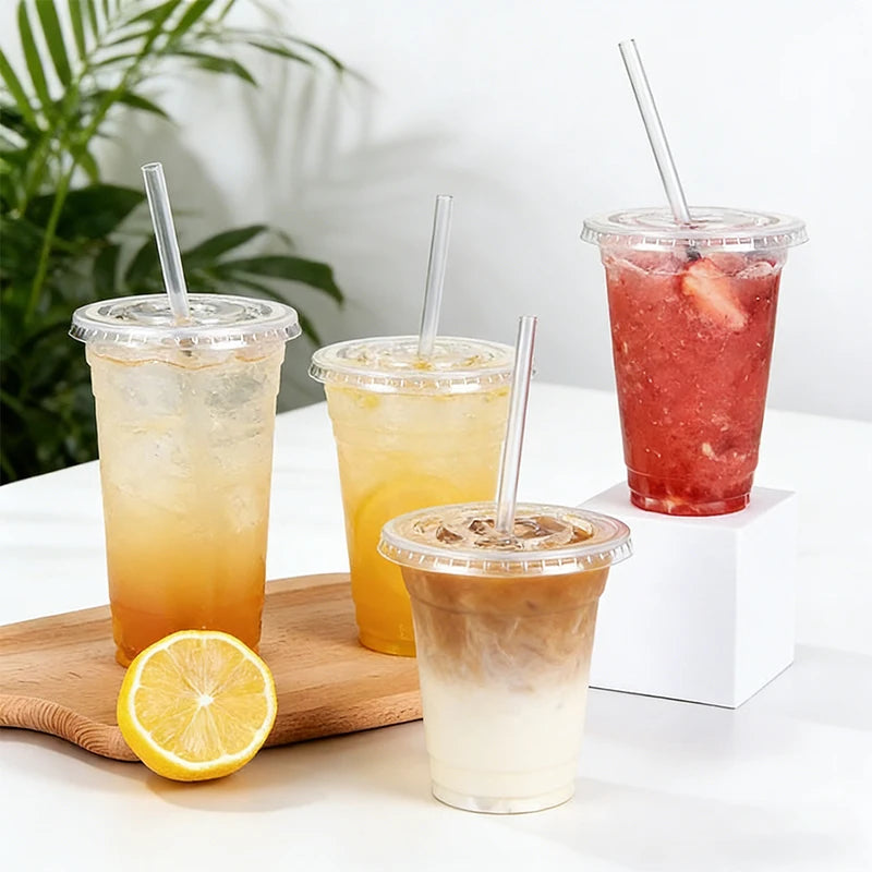 A collection of iced beverages in clear plastic cups with straws and lids, including orange, yellow, and pink drinks.
