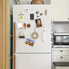 A white refrigerator door decorated with various magnetic acrylic picture frames, a clock, and decorative elements.