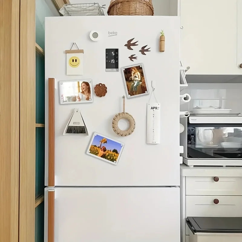 A white refrigerator door decorated with various magnetic acrylic picture frames, a clock, and decorative elements.