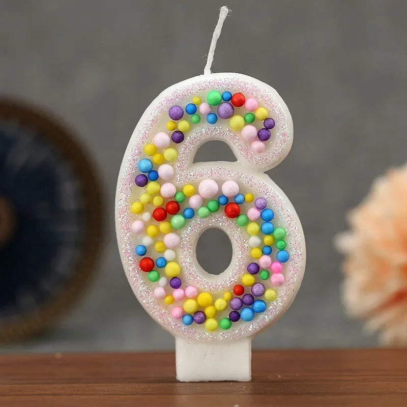 A white candle shaped like the number six decorated with colorful glitter candy beads