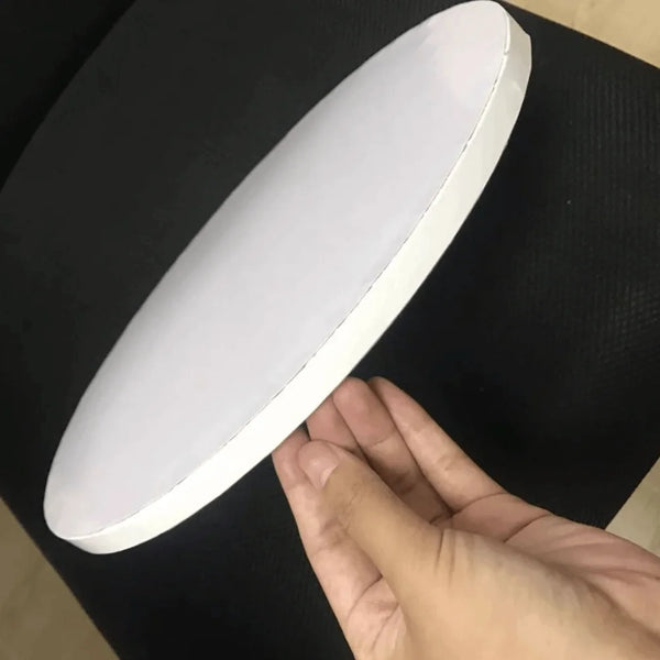 A white, oval-shaped piece of corrugated cake board is held by a hand against a black surface.