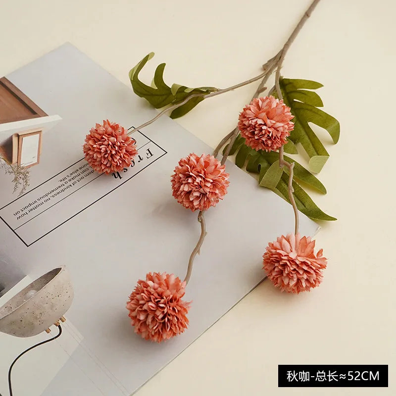 A sprig of artificial pink chrysanthemum pompon flowers with green leaves displayed on a white background.