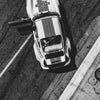 Photo noir et blanc d'une voiture classique blanche vintage, probablement une Porsche, garée sur de l'asphalte.