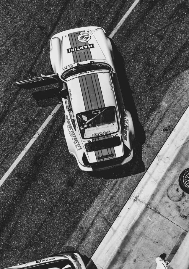 Photo noir et blanc d'une voiture classique blanche vintage, probablement une Porsche, garée sur de l'asphalte.