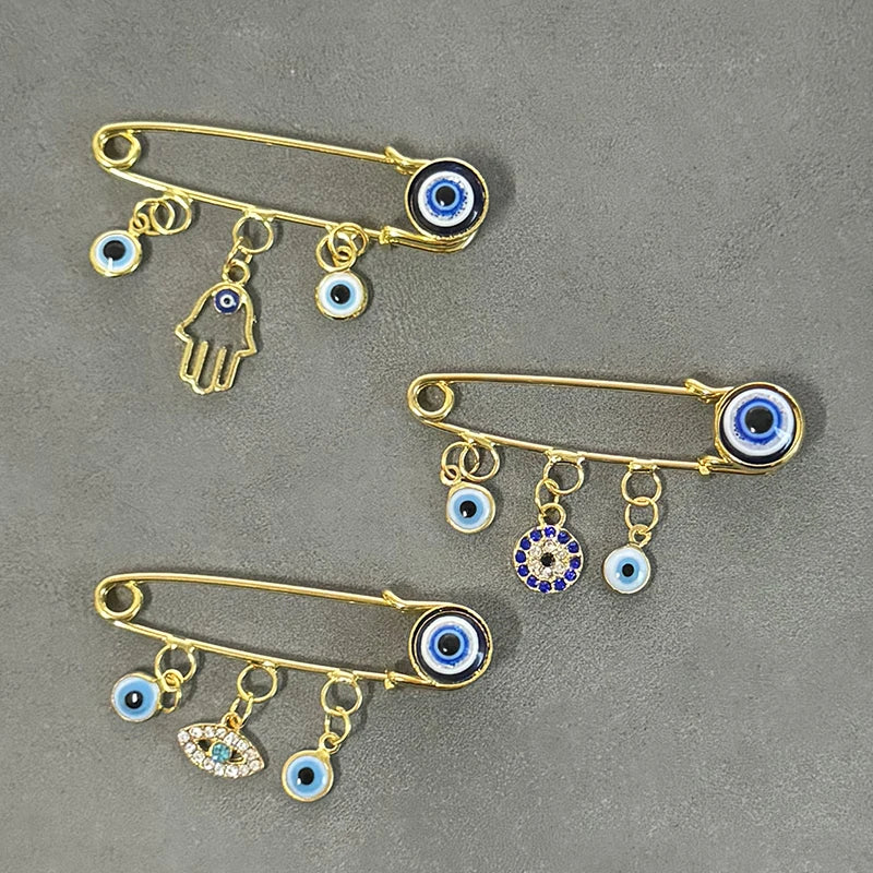 Elegant gold and silver evil eye brooch pin featuring various eye motifs and dangling charms.