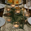 Gold glass tealight candle holders arranged on a lace tablecloth with green foliage.