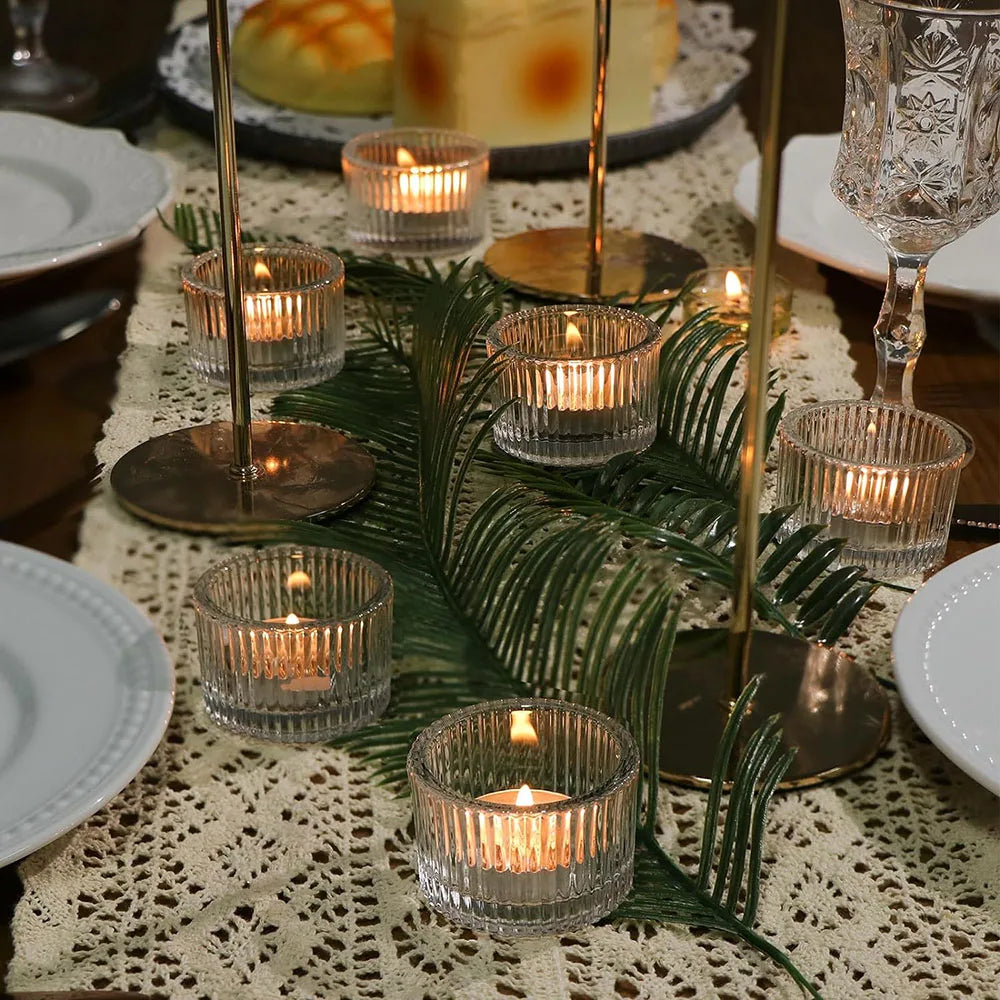 Gold glass tealight candle holders arranged on a lace tablecloth with green foliage.