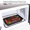 A black food storage container with meat and vegetables is placed inside a white microwave oven compartment.