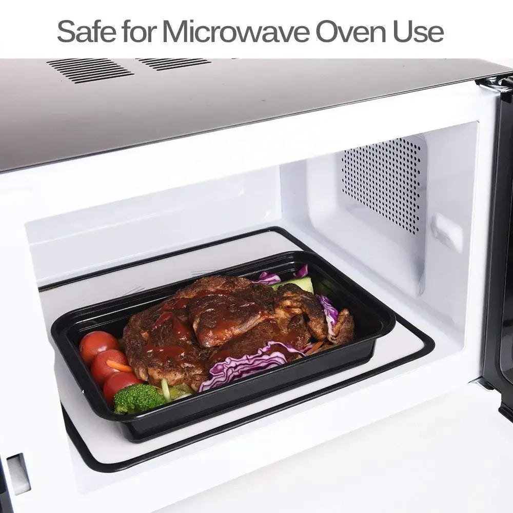 A black food storage container with meat and vegetables is placed inside a white microwave oven compartment.