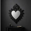 A black ornate flame wall mirror with a heart-shaped reflection mounted on a dark gray wall.