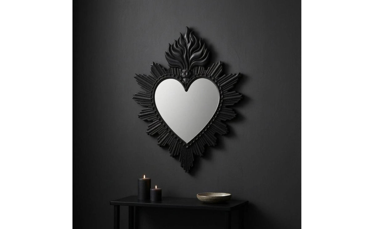 A black ornate flame wall mirror with a heart-shaped reflection mounted on a dark gray wall.