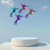 A group of iridescent hummingbird wall art featuring vibrant greens, purples, and pinks against a light blue sky.
