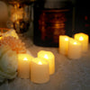 A collection of glowing yellow LED tea light candles arranged on a lace cloth with blurred background elements.