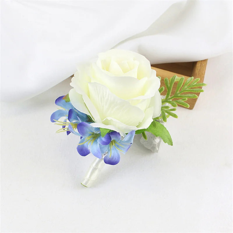 A boutonniere set featuring a white rose and blue flowers with green foliage displayed on a light background.
