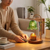 A person is using an adjustable height aromatherapy candle warmer lamp with a green glass shade on a wooden table.
