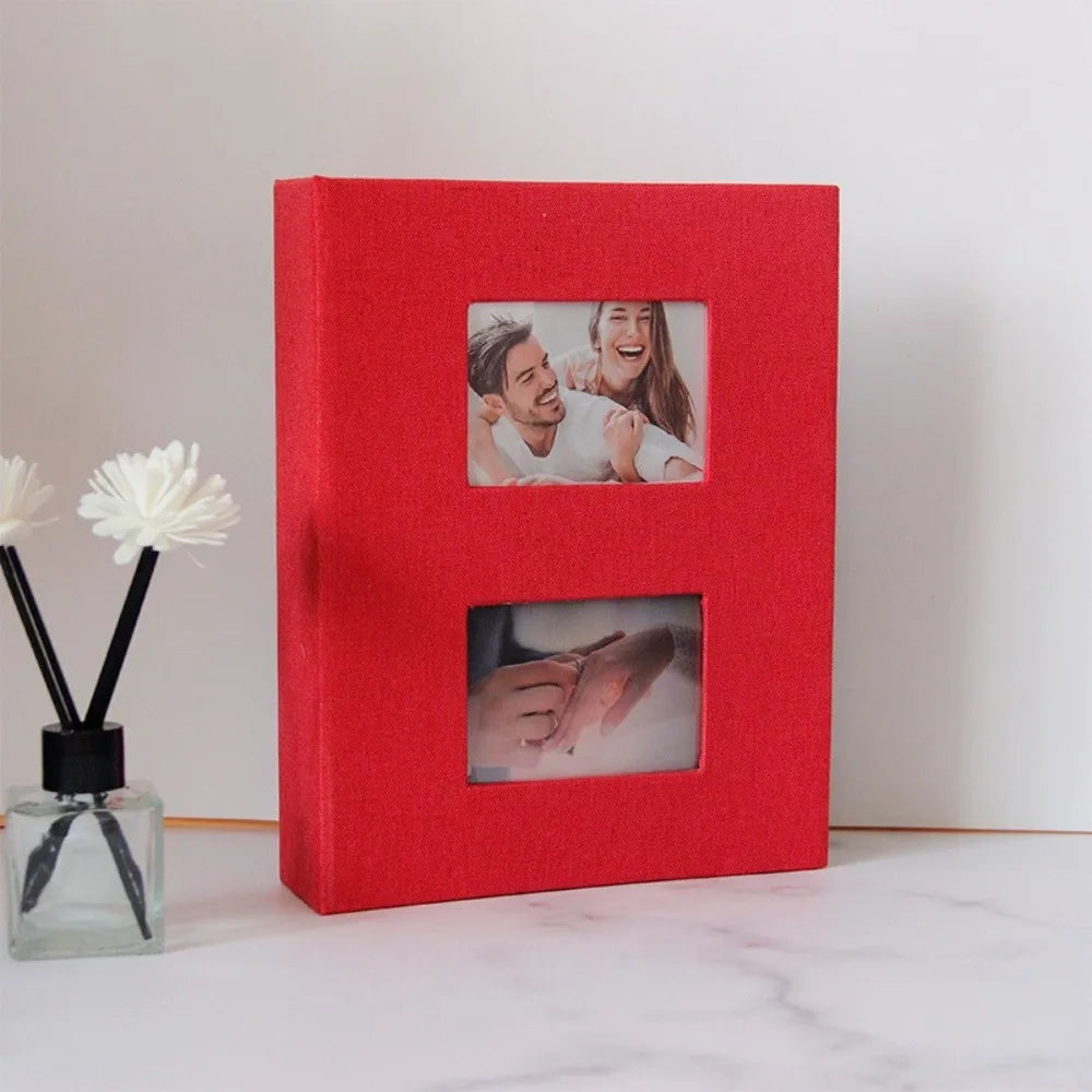 A red linen-cover photo album with two visible photo pockets showing a couple.