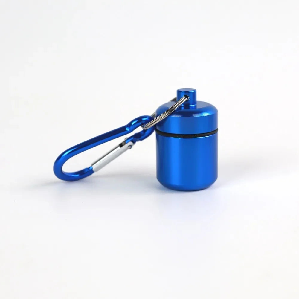 A small, blue waterproof pill organizer is attached to a silver keychain ring.
