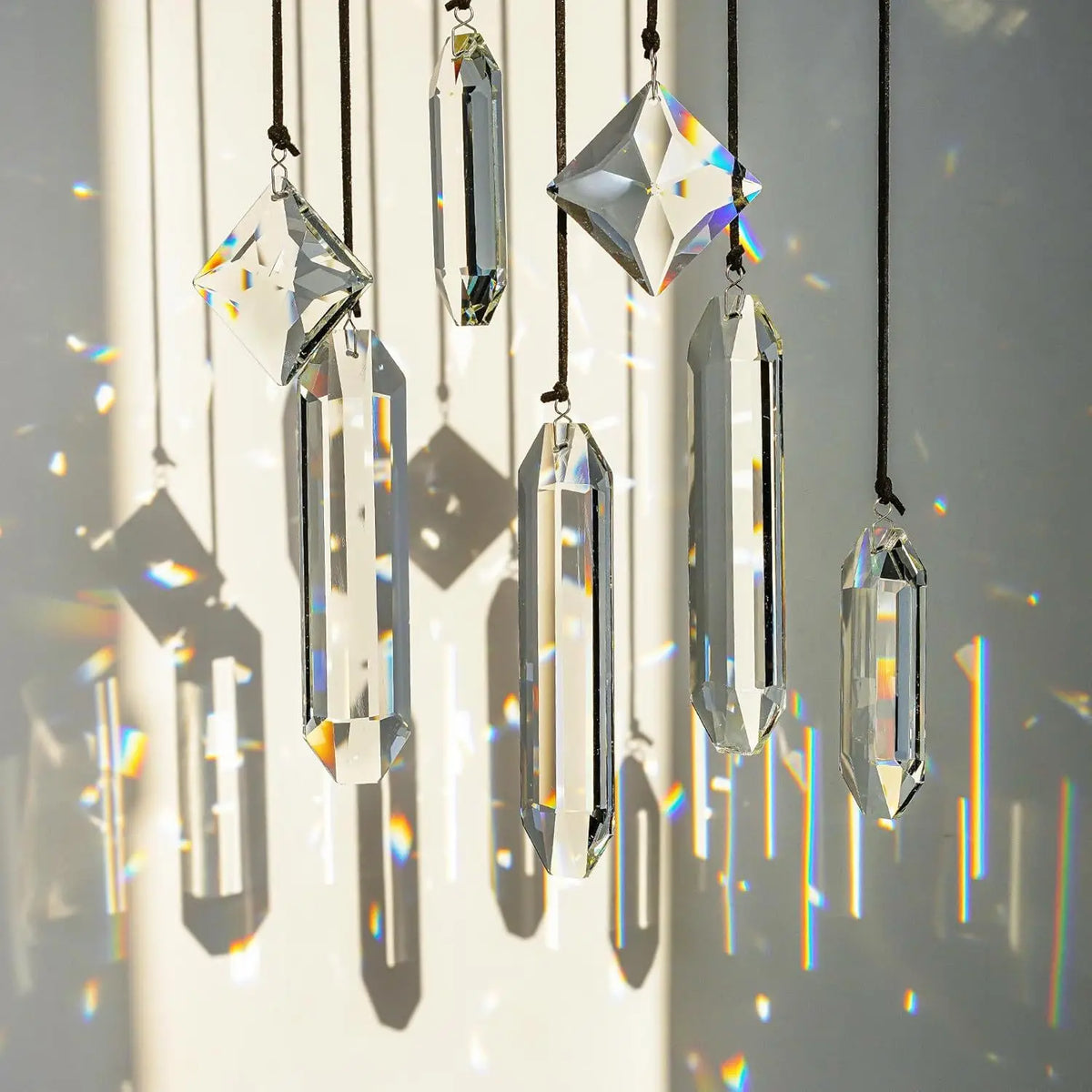 A set of seven crystal prism sun catchers hanging vertically, casting colorful light patterns on a white surface.